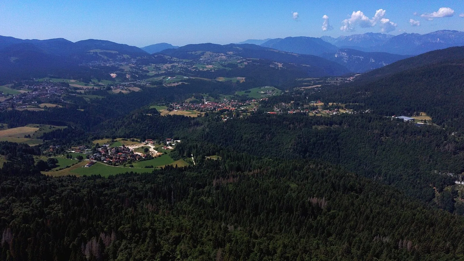 Veduta aerea dell'Altopiano di Asiago con boschi di conifere, prati, piccoli centri abitati e le montagne sullo sfondo