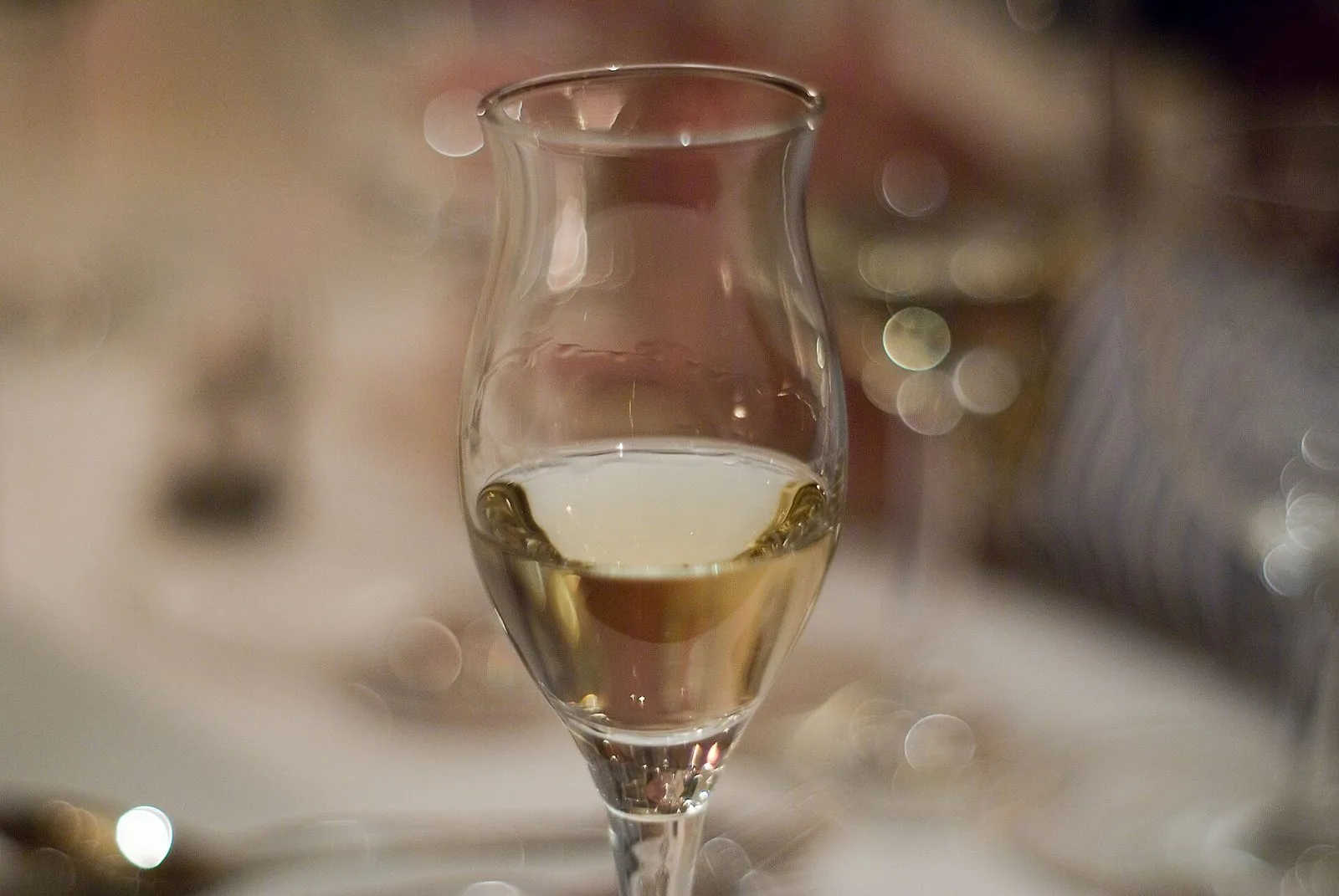 Calice a tulipano con grappa dal riflesso dorato su una tavola, sfondo sfocato