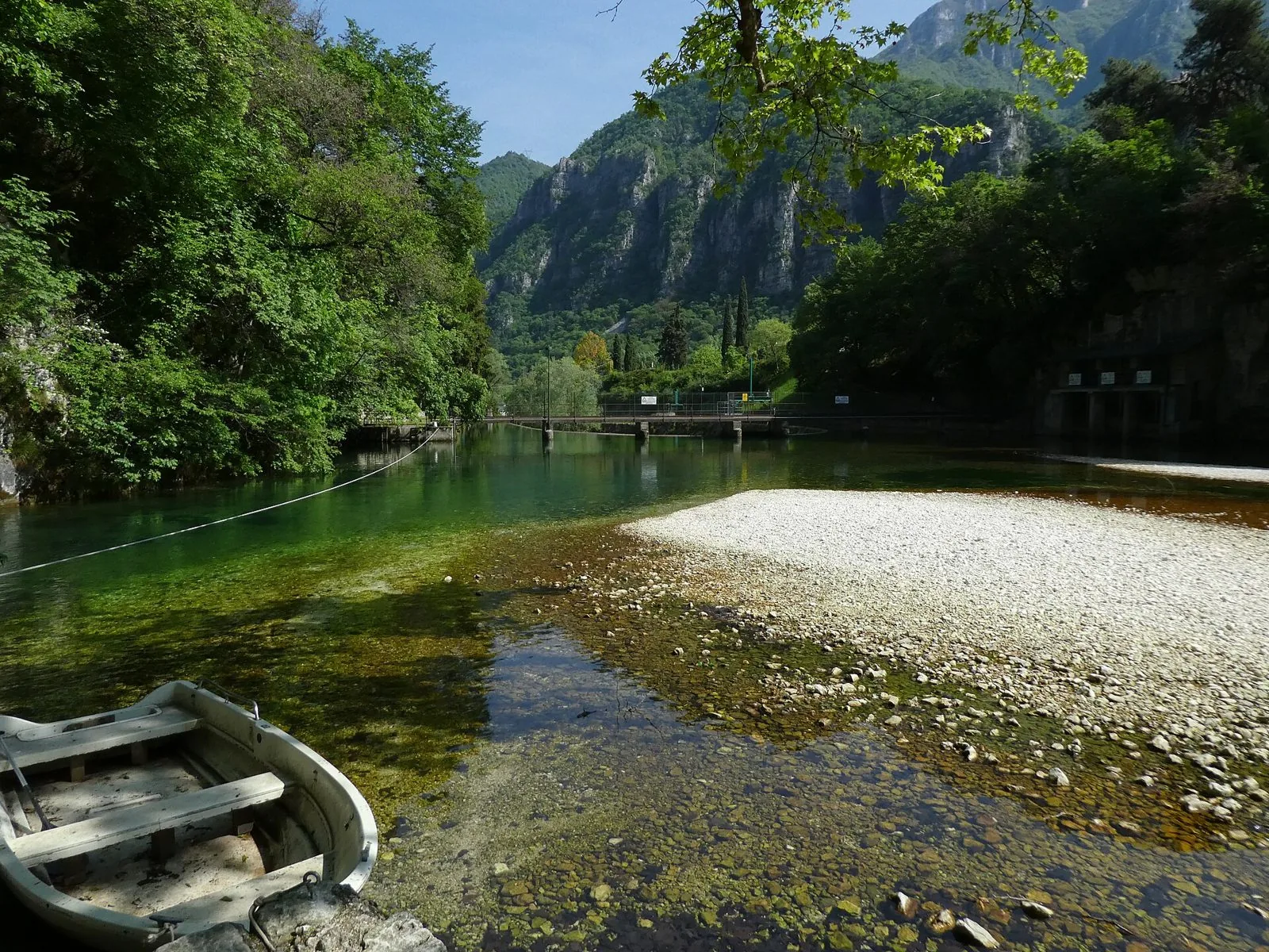 Le acque verde smeraldo dell'Oliero nel parco naturale delle Grotte di Oliero, con una barca sulla riva e le pareti rocciose della valle sullo sfondo