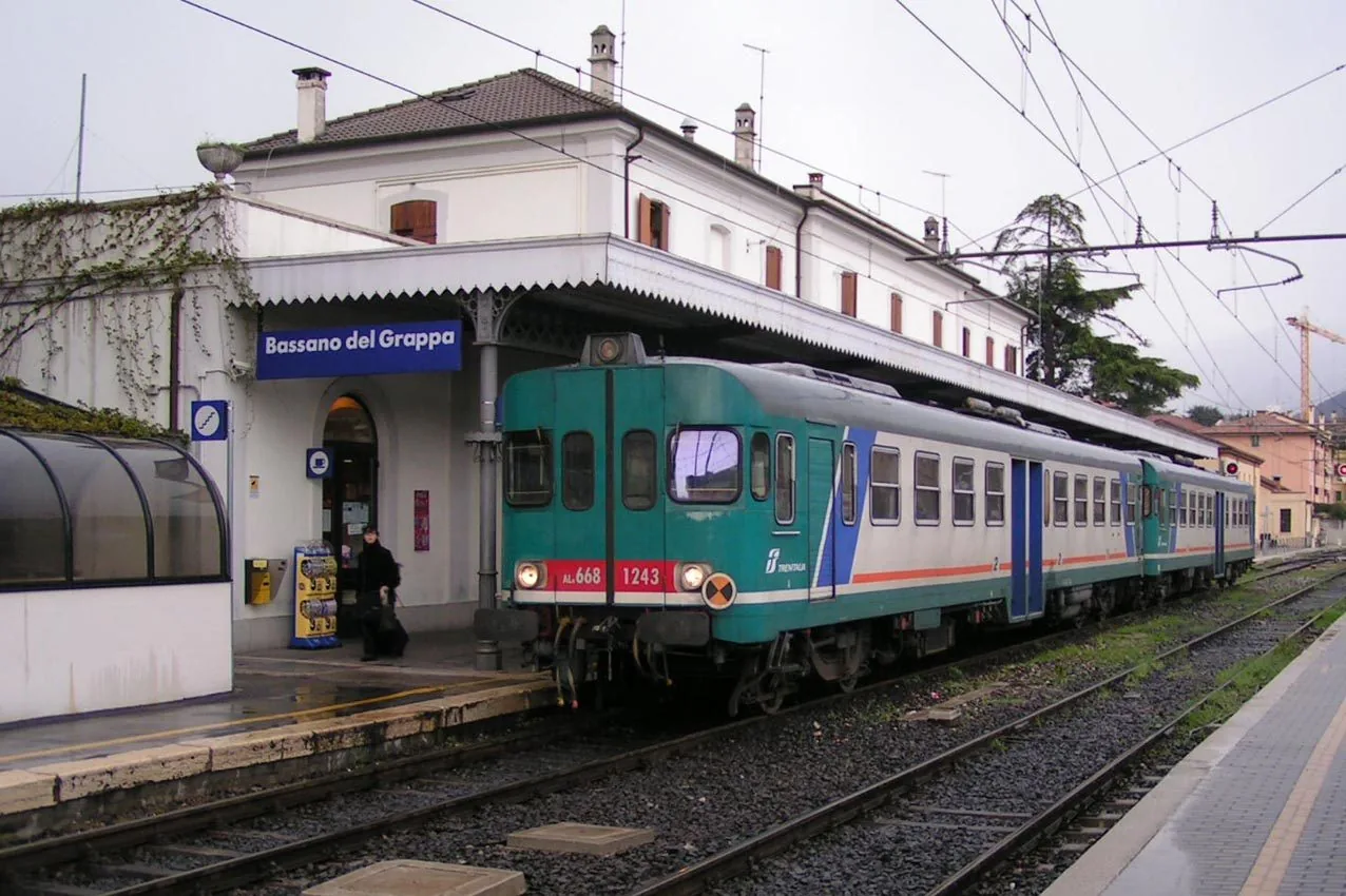 Treno regionale fermo al binario della stazione di Bassano del Grappa, con l'insegna blu della stazione sulla facciata